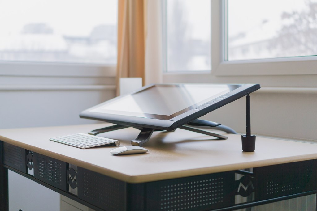 An artist's workspace featuring a digital drawing tablet, keyboard, and mouse on a desk near a window.