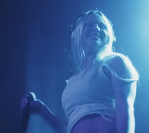 DJ_Dave smiling on stage under blue lighting, holding a microphone.