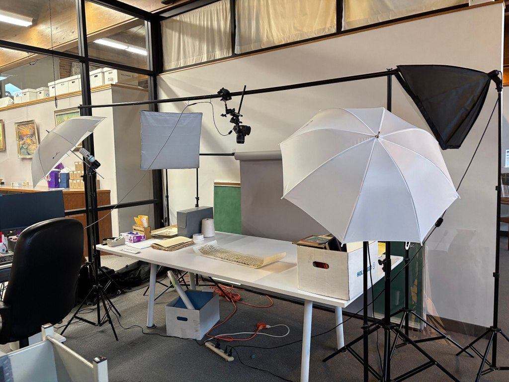 A photography setup featuring a table with a keyboard, a white backdrop, and multiple studio lights, including umbrella lights, in a workspace.